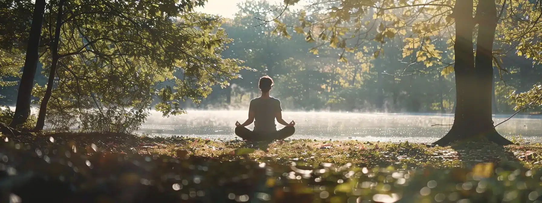 a person peacefully meditating by a serene lake, surrounded by gentle nature sounds and soft sunlight filtering through the trees.